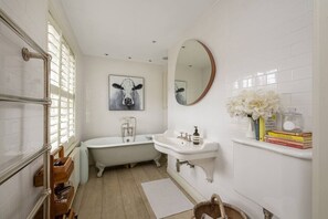 Un baño con una bañera, un lavabo, un espejo y un cuadro de una vaca en la pared.