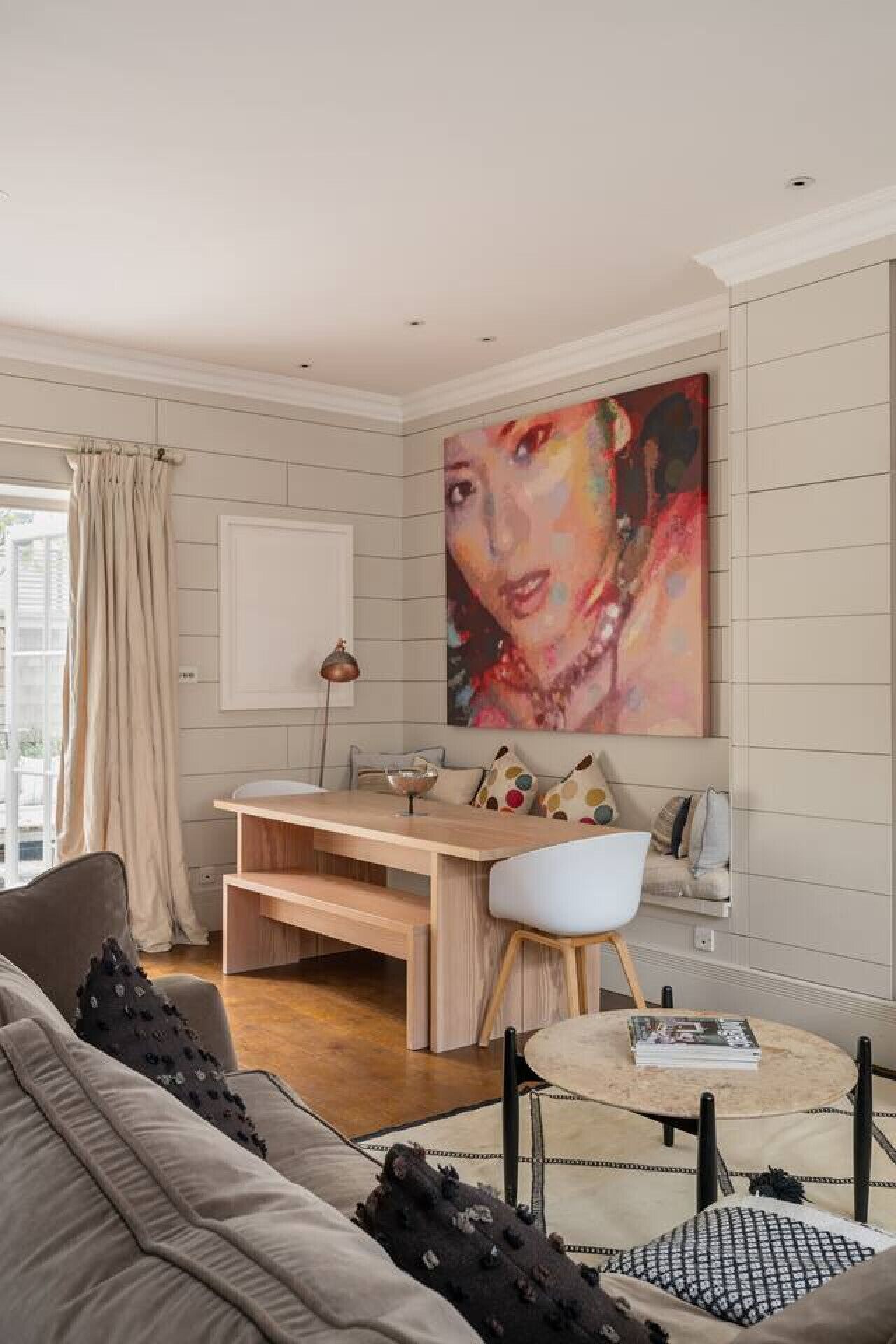 A modern living room with a grey sofa, a round coffee table, a wooden desk, and a large abstract painting on the wall.