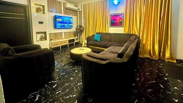 Una sala de estar moderna con piso de mármol negro, un sofá, un televisor y cortinas doradas.