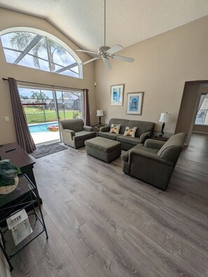 A spacious living room with a large window, a ceiling fan, and a pool view. - LKB4705AW 4 Bedroom villa in Lake Berkley 4 Home (Kissimmee)