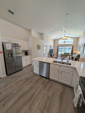 A kitchen with white cabinets, a stainless steel refrigerator, a dishwasher, and a large window providing natural light. - LKB4705AW 4 Bedroom villa in Lake Berkley 4 Home (Kissimmee)