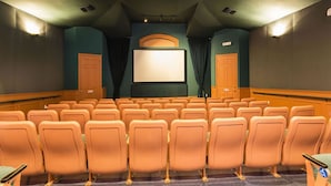 Ein Kino mit Reihen orangener Sitze, einer großen Leinwand und einem Projektor.