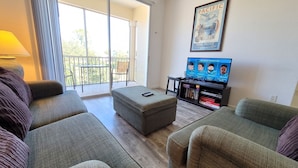 Ein Wohnzimmer mit einer Couch, einem Hocker und einem Fernseher, der Sportnachrichten zeigt.