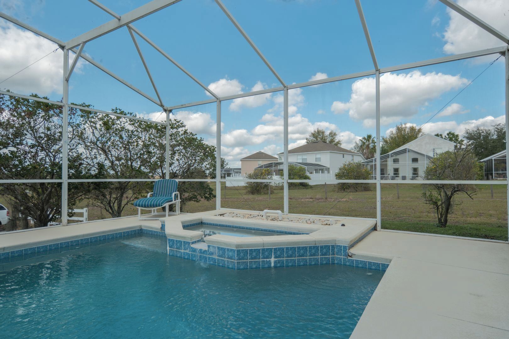 A swimming pool with a hot tub, a covered patio, and a view of houses in the background.