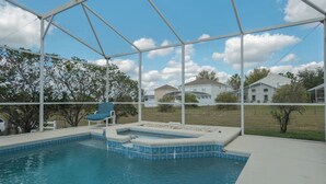Uma piscina com hidromassagem, um alpendre coberto e vista para casas ao fundo.