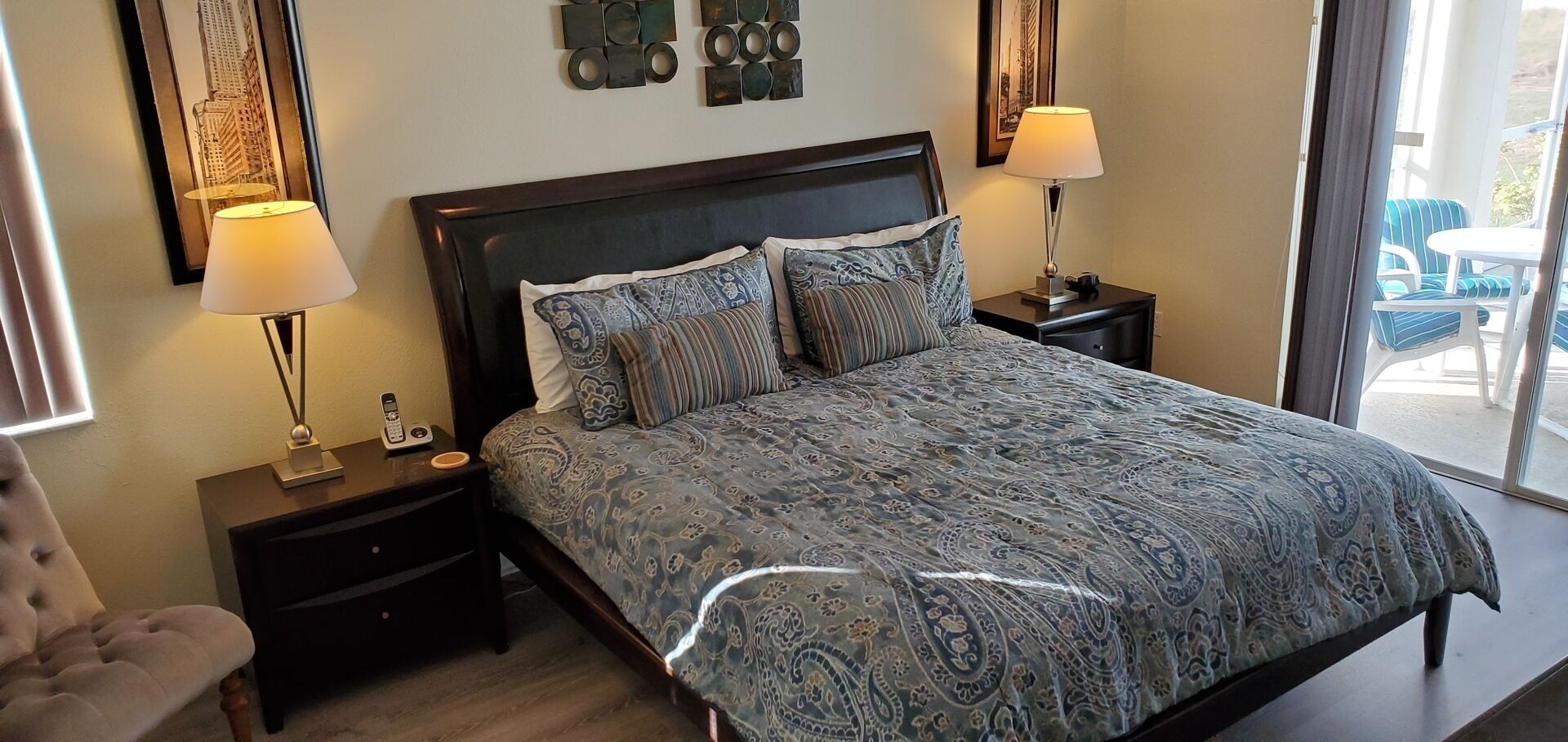 Une chambre avec un grand lit, deux tables de chevet avec des lampes, un fauteuil et une vue sur l’extérieur.