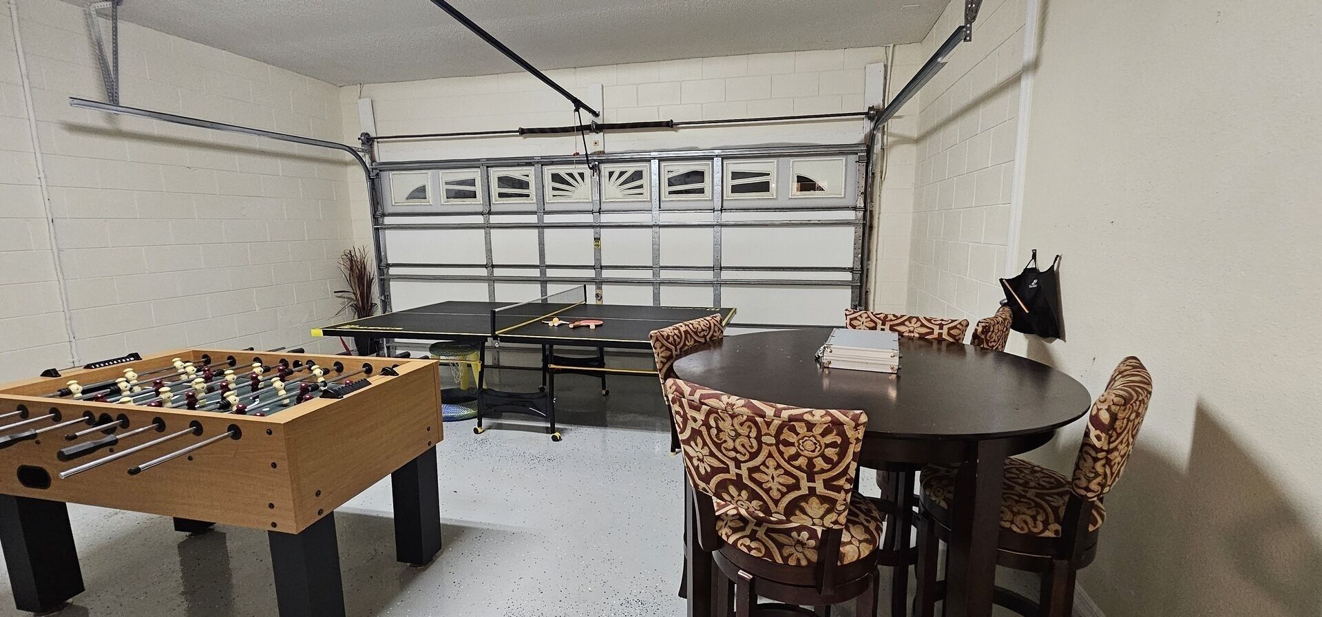Une pièce comprenant un baby-foot, une table de ping-pong et quatre chaises à motifs disposées autour d’une petite table.