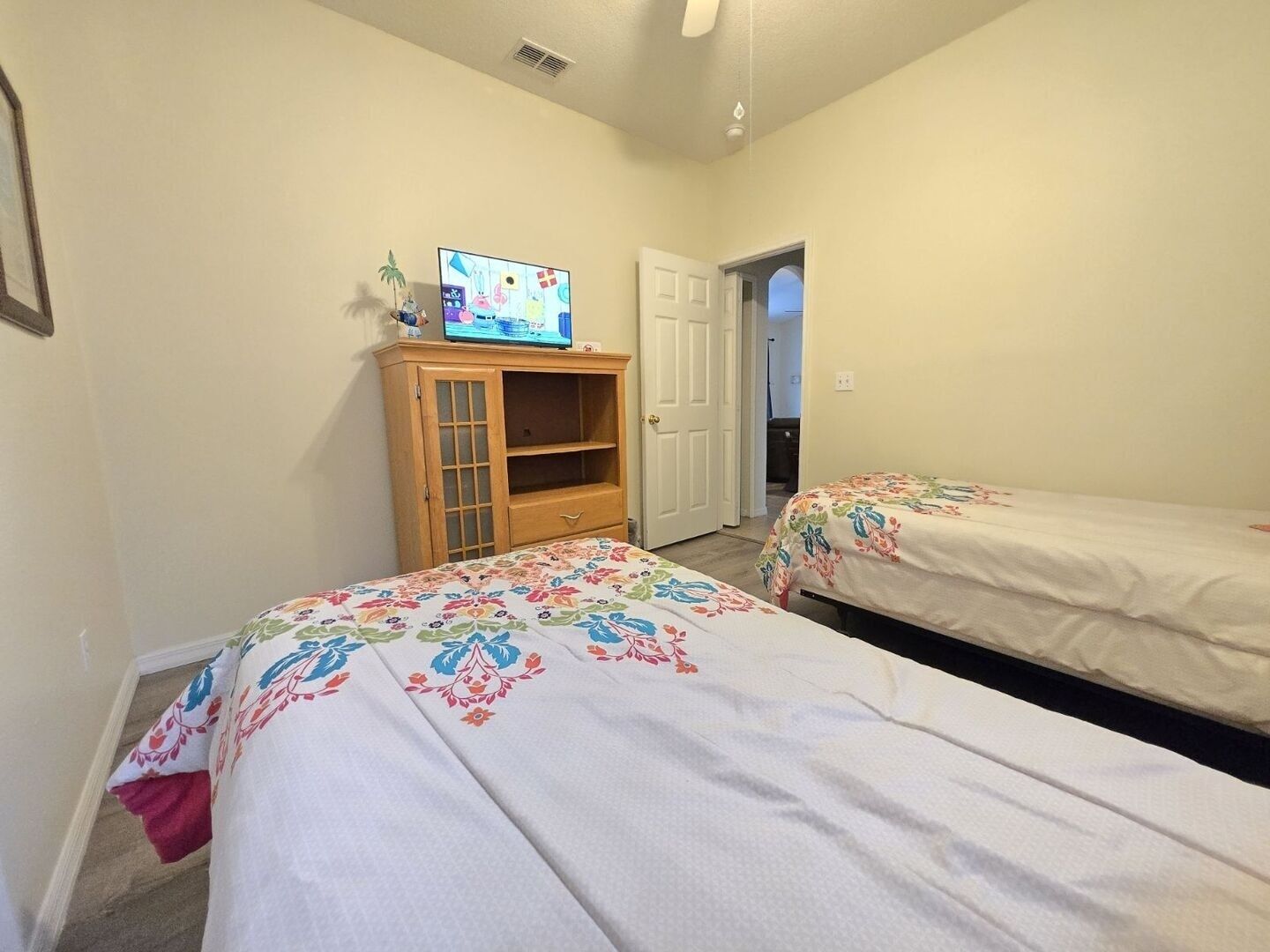 Ett sovrum med två sängar, ett träskåp med en tv och en dörr som leder till ett annat rum.