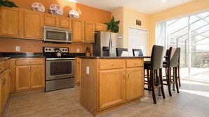 A modern kitchen with wooden cabinets, stainless steel appliances, and a large island with bar stools. - Sol142ca Spectacular 6 Bed, Solana Commuity Villa 6 Bedroom Home (Davenport)