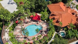 Vista aérea de un complejo turístico con una piscina central, rodeado de palmeras y edificios con tejados rojos.