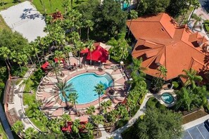 Eine Vogelperspektive eines Resorts mit einem zentralen Schwimmbecken, umgeben von Palmen und Gebäuden mit roten Dächern.