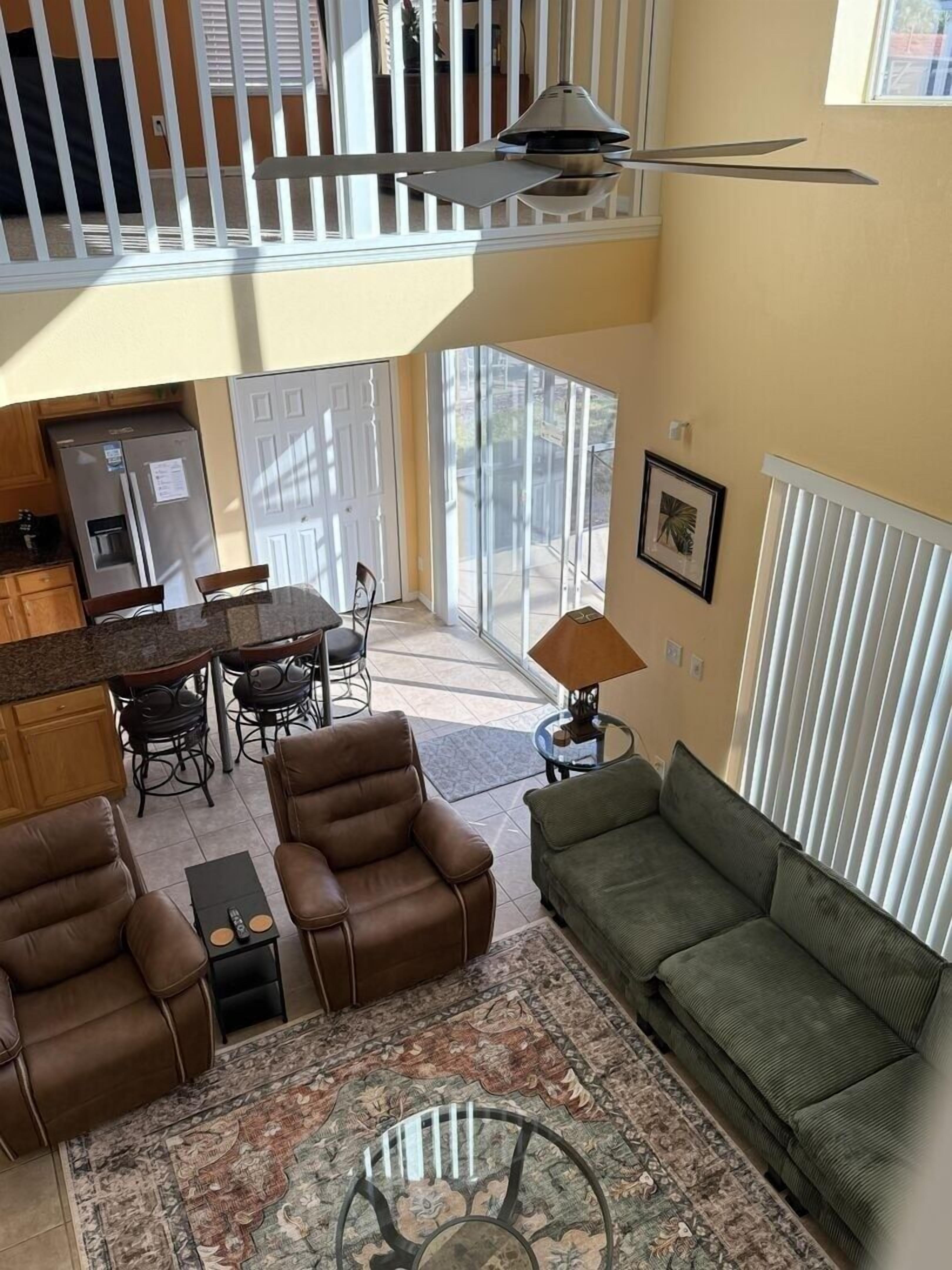 A spacious living area with a high ceiling, a dining table, multiple chairs, a sofa, a coffee table, and a ceiling fan.