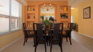 A dining area with a table set for six, surrounded by chairs with woven backs. There are shelves above the table holding decorative items and a chandelier hanging from the ceiling. - Sol142ca Spectacular 6 Bed, Solana Commuity Villa 6 Bedroom Home (Davenport)