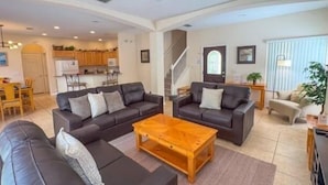 A spacious living room with two sofas, a coffee table, and a TV. There is a kitchen in the background with cabinets and a dining area. - HG423SP 4 Bedroom villa in High grove 4 Home (Clermont)