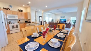 A modern kitchen with a dining area, featuring a central island, wooden chairs, and a television in the background. - HG423SP 4 Bedroom villa in High grove 4 Home (Clermont)