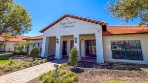A building with a sign reading 'Ditch Grove Clubhouse,' featuring a red-tiled roof, white walls, and a covered entrance with columns. - HG423SP 4 Bedroom villa in High grove 4 Home (Clermont)