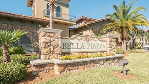 Une enseigne en pierre sur laquelle est inscrit « Bella Pizzeria », entourée de verdure et de palmiers.