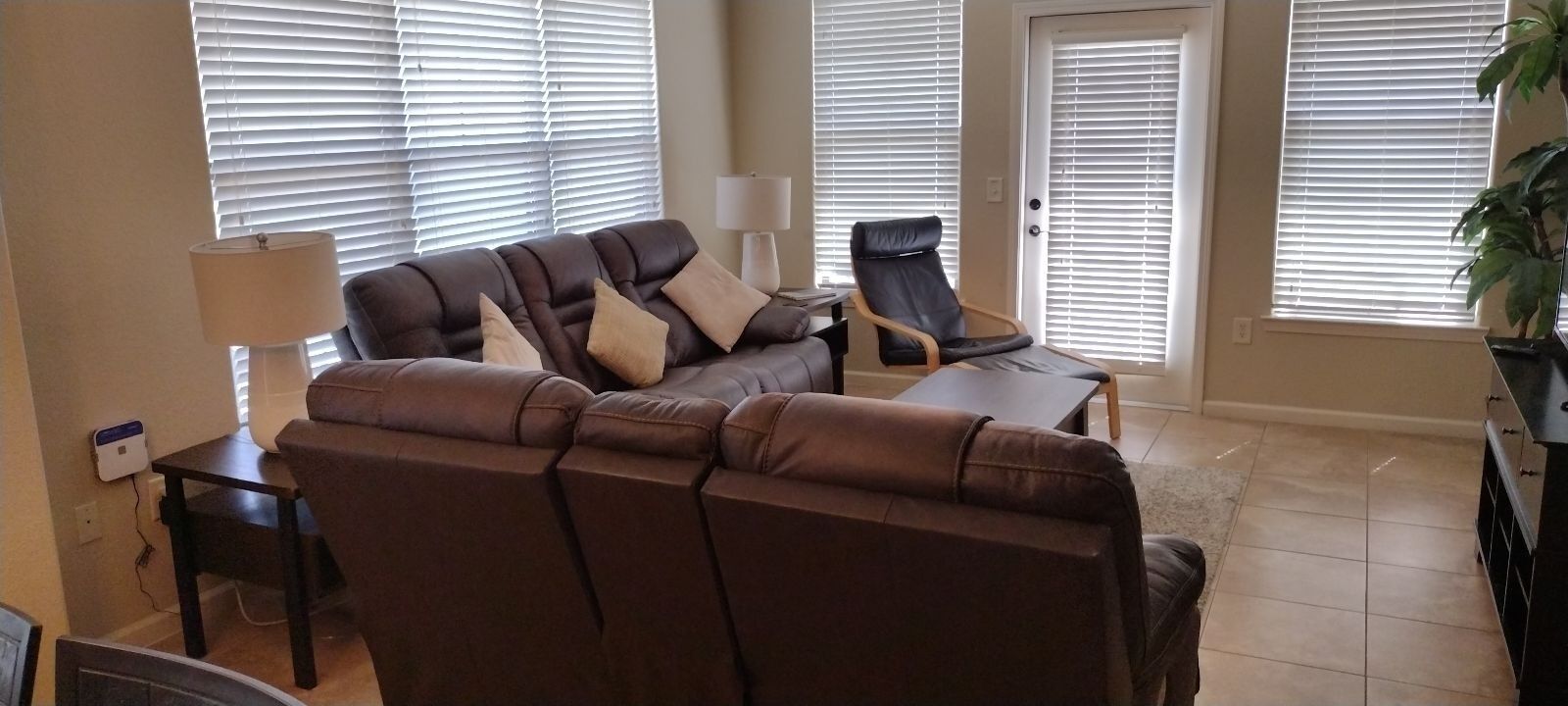 Una sala de estar con un sofá marrón, una mesita, una silla y una lámpara.