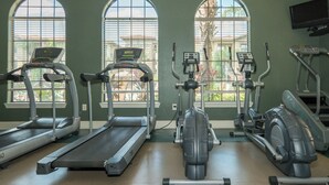 Une salle de sport équipée de tapis de course, de vélos elliptiques et de vélos d’appartement, avec de grandes fenêtres donnant sur un quartier résidentiel.