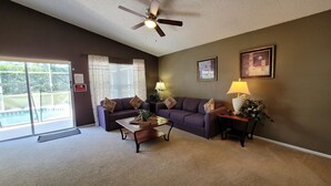 A living room with a sofa, coffee table, and lamps. There is a ceiling fan and a door leading to a balcony. - HL740BD 4 Bedroom Villa in Hampton Lakes 4 Home (Davenport)
