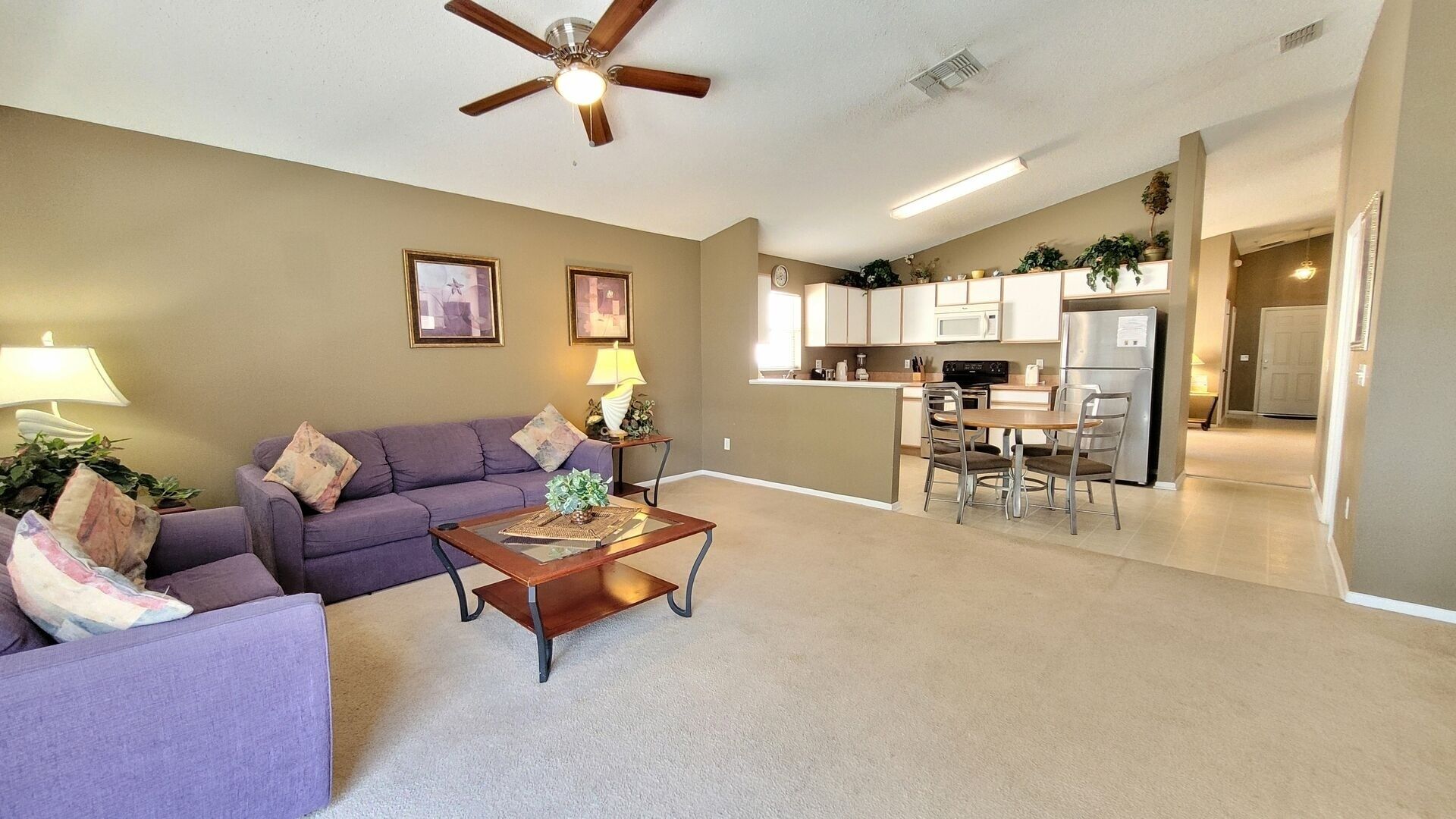 A living room with a purple sofa, a wooden coffee table, and a ceiling fan.