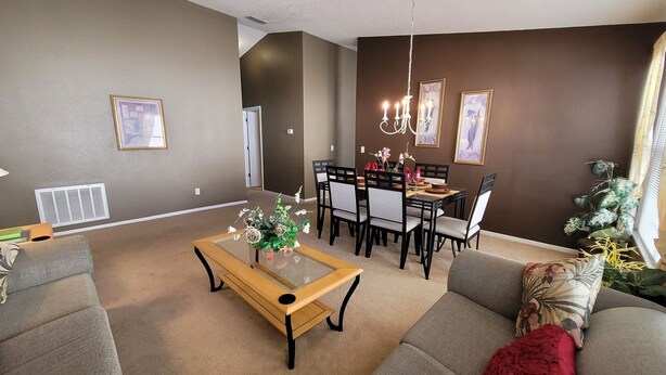 A living room with a sofa, a coffee table, a dining table with chairs, and a chandelier. - HL740BD 4 Bedroom Villa in Hampton Lakes 4 Home (Davenport)