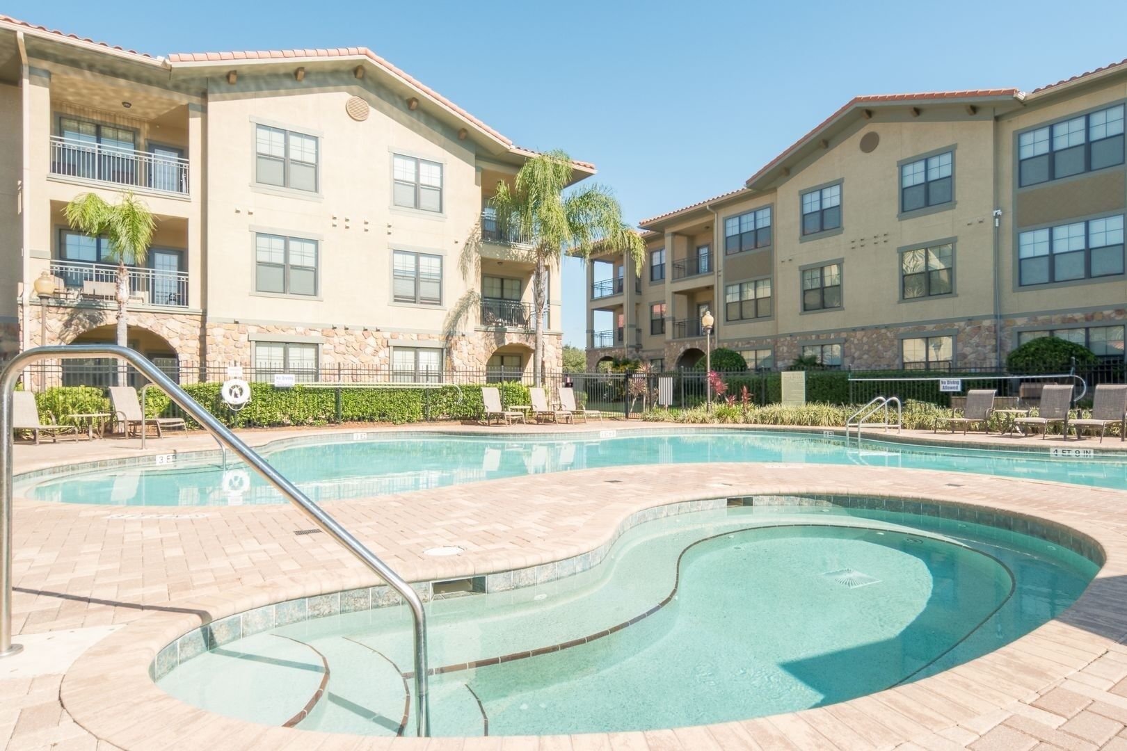 Un espace piscine avec des chaises longues et un bâtiment doté de nombreux balcons.