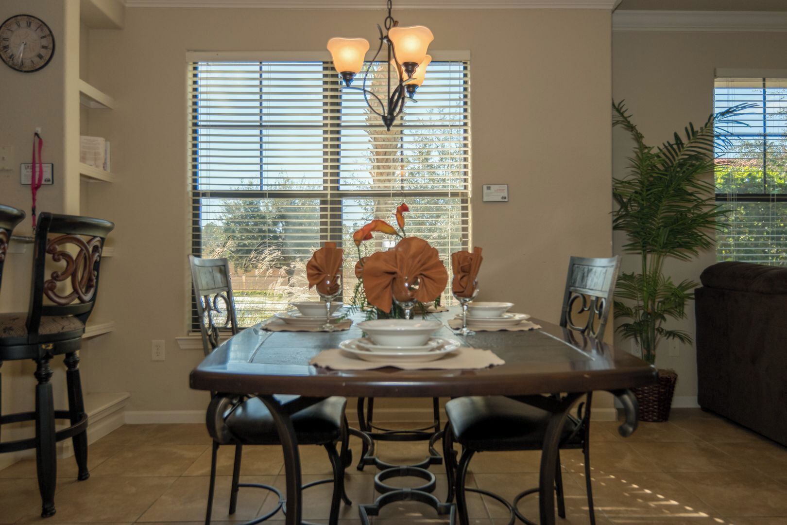 A dining area with a table set for four, chairs, a chandelier, and a window with blinds.