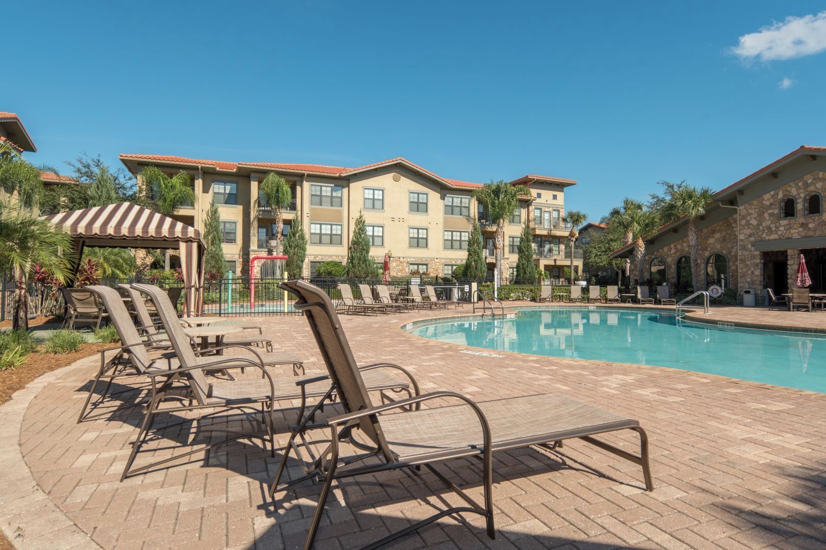 A swimming pool area with lounge chairs and a building with multiple balconies in the background.