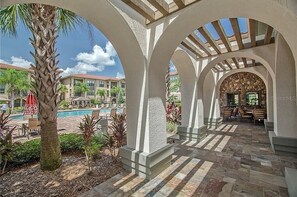 A covered outdoor area with stone flooring, palm trees, and a pool in the background. - BP914CP 3 Bedroom Condo in Bella Piazza 3 Condo (Davenport)