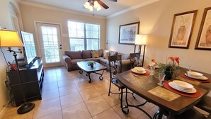 A dining area with a table set for four, a sofa, and a television in the background. - BP835CP 4 Bedroom Condo in Bella Piazza 4 Condo (Davenport)