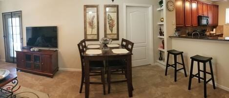 A dining area with a table and chairs, a television, and a kitchen area with cabinets and stools.