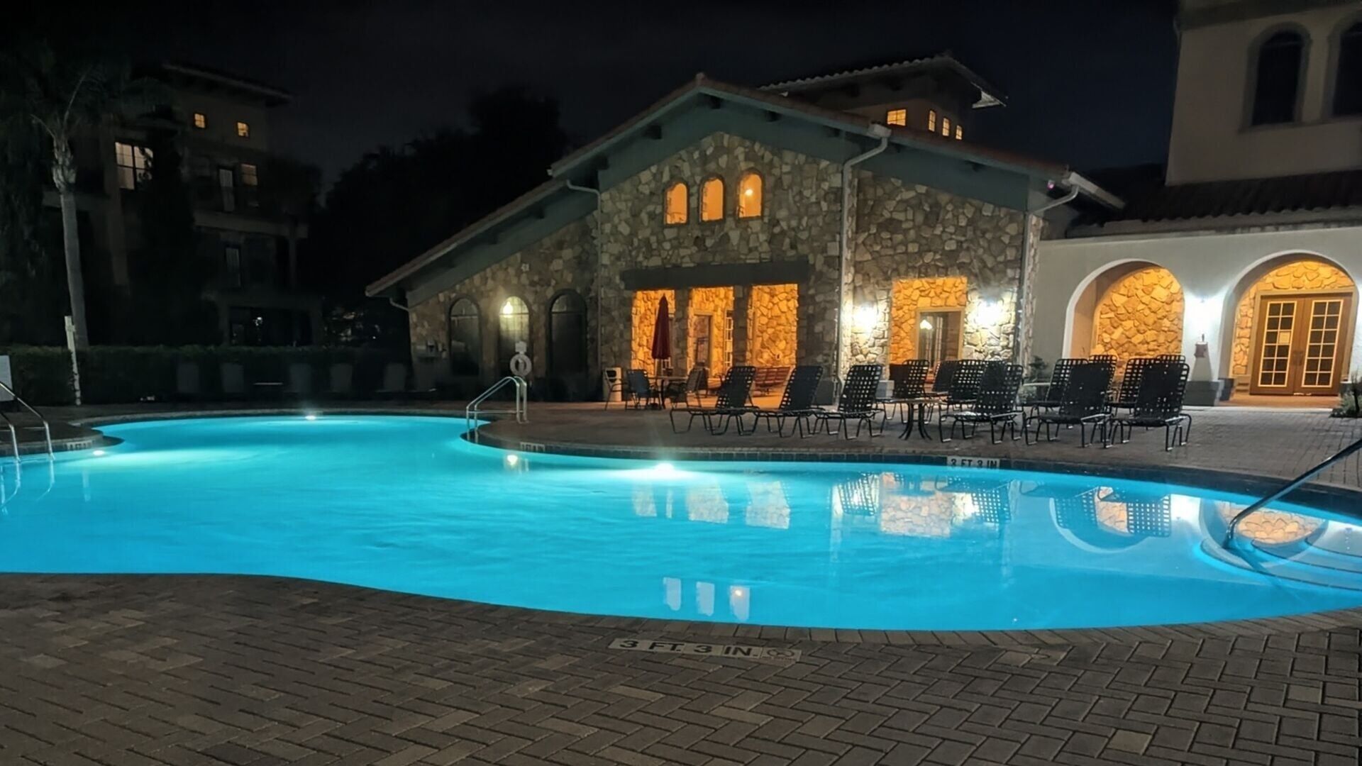 Una piscina con sillas de descanso y un edificio de piedra con ventanas arqueadas.