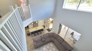 A spacious living area with a large gray sectional sofa, a kitchen with modern appliances, and a view of the outside through a large window. - Sol1520sc 6 Bed Solana Holiday Villa 6 Bedroom Home (Davenport)