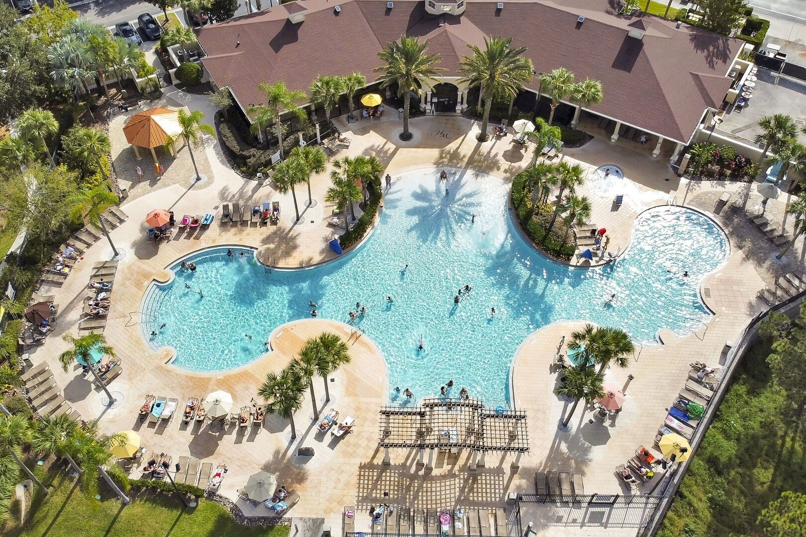 An aerial view of a resort with a large central pool, multiple smaller pools, and a variety of sun loungers and umbrellas.