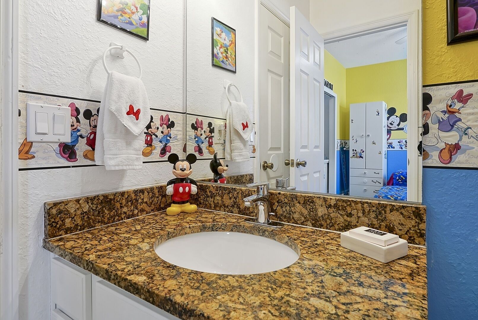 Un baño con decoración de Mickey Mouse, encimera de granito y un lavabo.