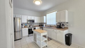 A modern kitchen with white cabinets, stainless steel appliances, a wooden countertop, and a tiled backsplash. - Cp641cd 4 Bedroom Home (Haines City)