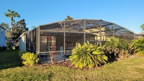 Une grande serre dotée d’un toit transparent, entourée d’une pelouse bien entretenue et de diverses plantes tropicales.