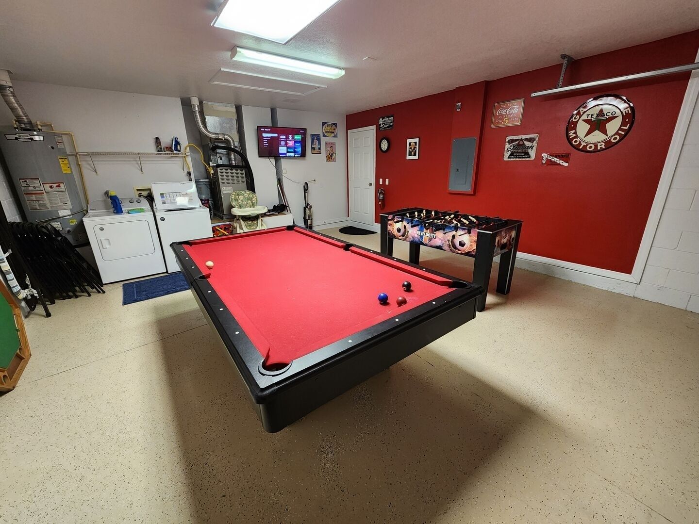 A billiards table in a room with a red wall, a washing machine, and a foosball table.