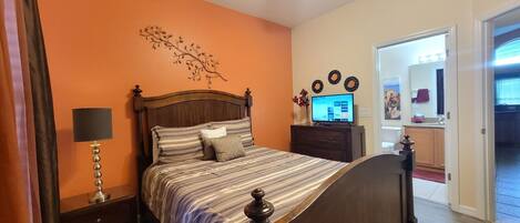 A bedroom with a bed, a nightstand, a lamp, a dresser, and a television.