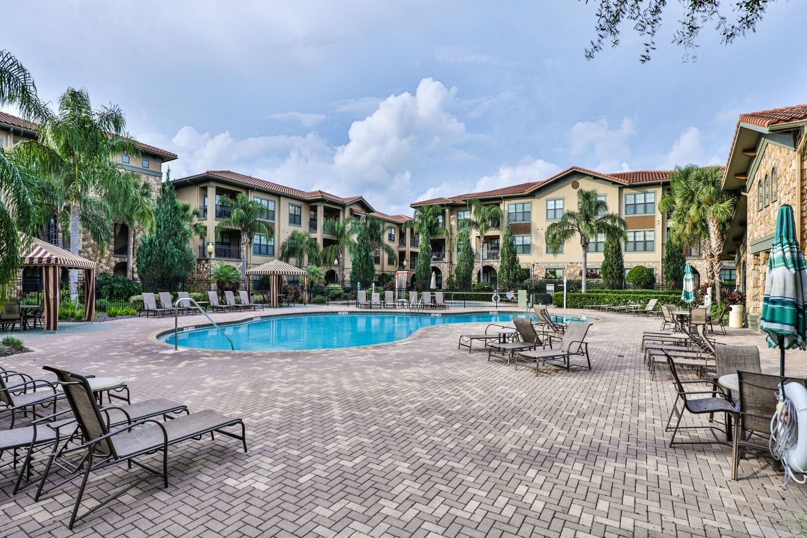 A pool area with lounge chairs and umbrellas, surrounded by multi-story buildings with balconies.