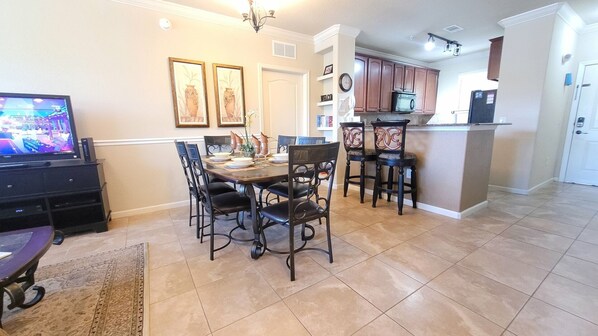 A dining area with a table and chairs, a kitchen with cabinets and appliances, and a television on a stand. - Bp421cp 3 Bed Condo At Bella 3 Bedroom Condo (Davenport)