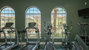 A gym with treadmills, ellipticals, and a stationary bike, with large windows offering a view of palm trees and buildings. - Bp421cp 3 Bed Condo At Bella 3 Bedroom Condo (Davenport)