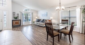 A spacious living area with a glass dining table, wooden chairs, a sofa, and a fireplace. - AV340RD 4 Bedroom Charming Villa in Aviana 4 Home (Davenport)