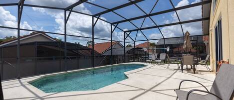 A covered outdoor swimming pool with a clear view of the surrounding houses and a patio area with chairs and umbrellas.