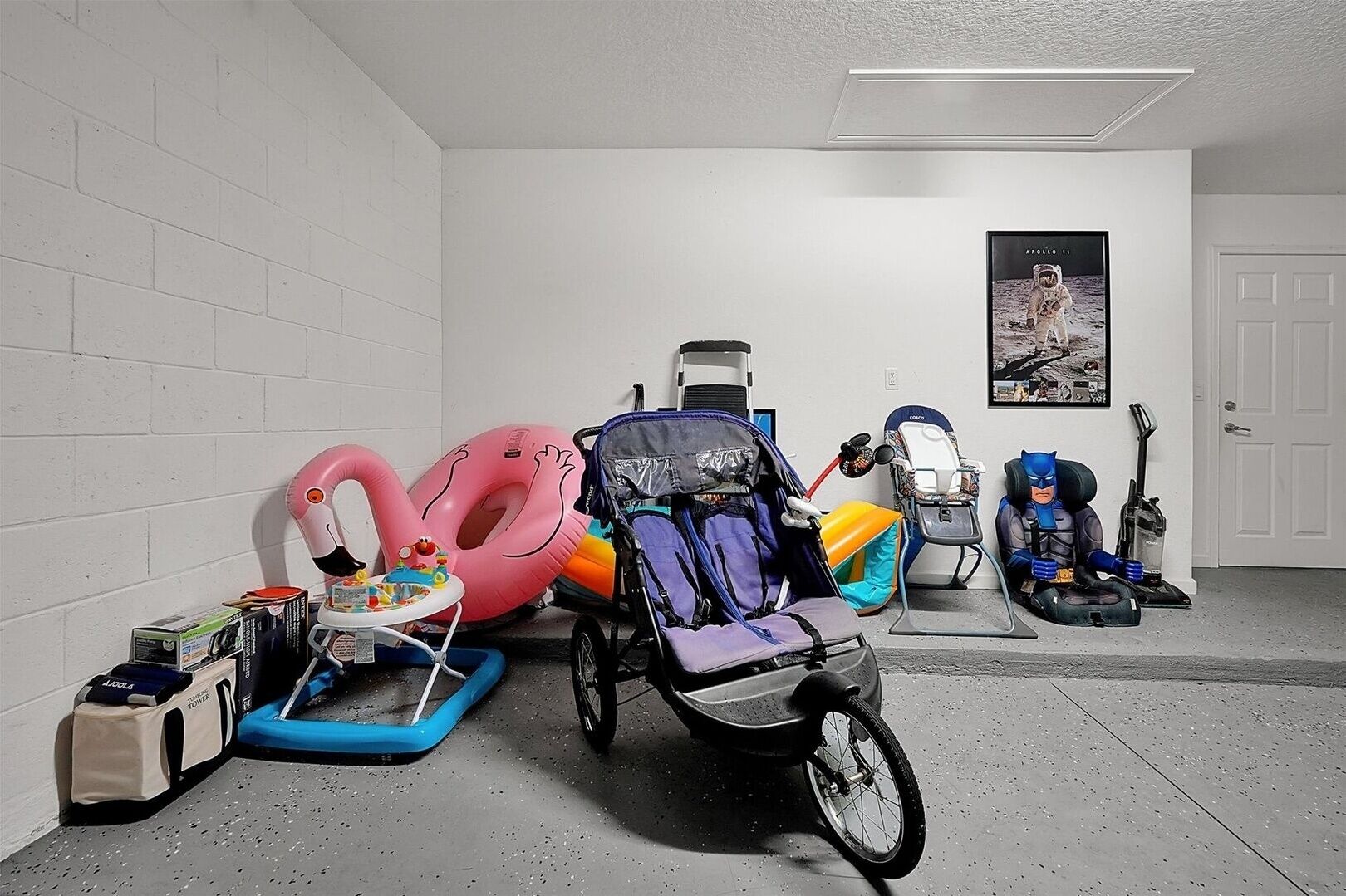 A room with a white brick wall, a baby stroller, a bicycle, and a poster of an astronaut on the wall.