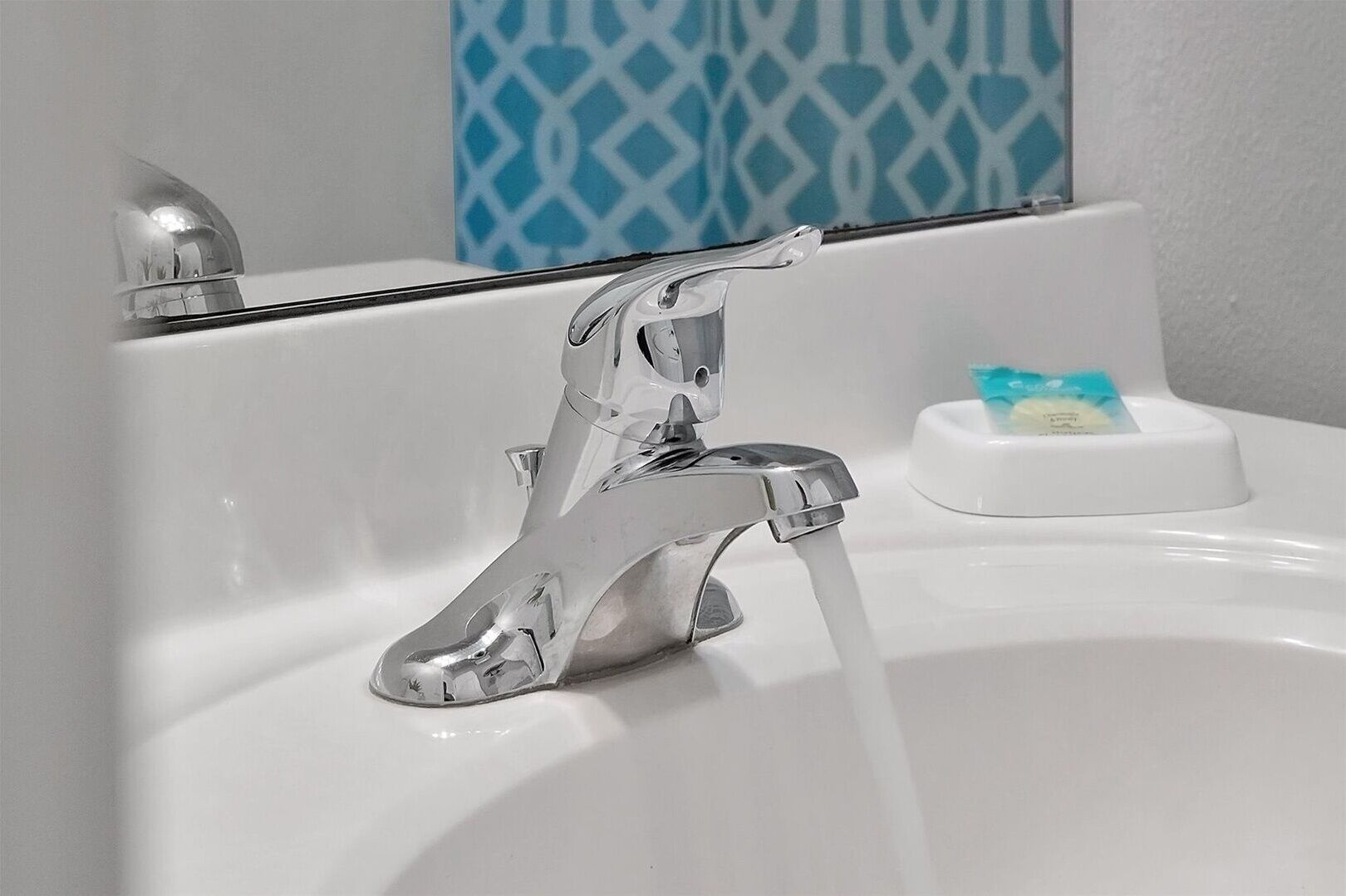 Un lavamanos con grifo de cromo, un jabonera y una pared azul con motivos decorativos al fondo.