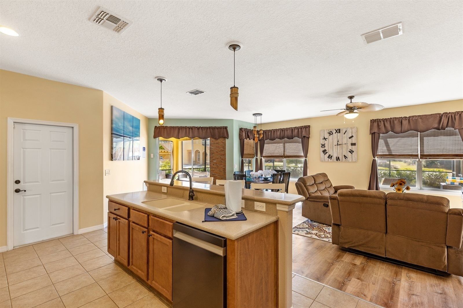 A modern kitchen with a built-in dishwasher, a dining area with a table and chairs, and a living room with a brown sofa and a ceiling fan.