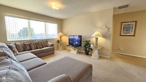 A living room with a sectional sofa, a flat-screen TV, two side tables with lamps, and a large window. - Cp938od 5 Bed Calabay Parc 5 Bedroom Home (Davenport)