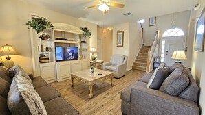 A living room with a TV, sofa, armchair, and a staircase. - Cp938od 5 Bed Calabay Parc 5 Bedroom Home (Davenport)